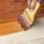 hand holding a brush applying varnish paint on a wooden surface